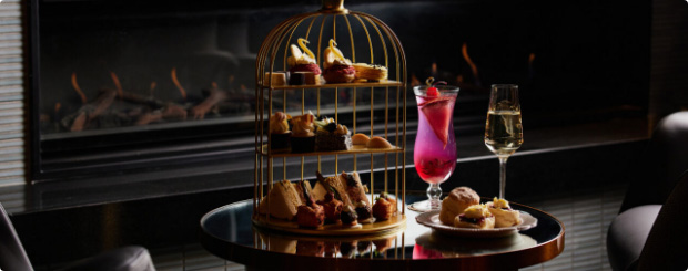 Indulge in The Birdcage Bar's high tea experience, featuring a birdcage full of pastries and sandwiches alongside creative cocktails by a cozy fireplace.