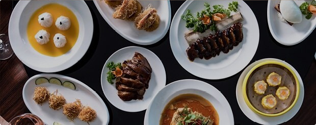 Spread of Chinese cuisine featuring dishes like dim sum, crispy pork belly and ribs on a dark table