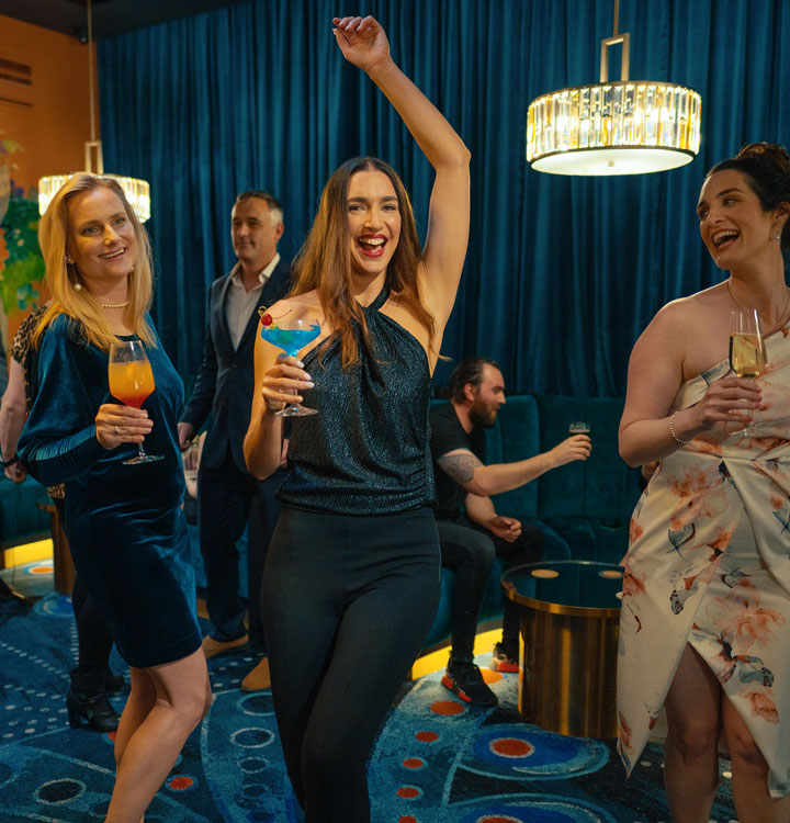 Vibrant scene at Wrest Point's Birdcage Bar with women enjoying cocktails and dancing, creating a lively atmosphere for a fun night out in Hobart.