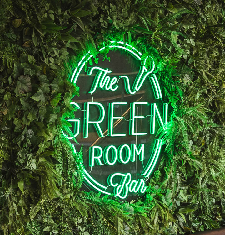 The Green Room Bar's glowing neon sign surrounded by a wall of greenery, inviting guests to a unique bar experience.