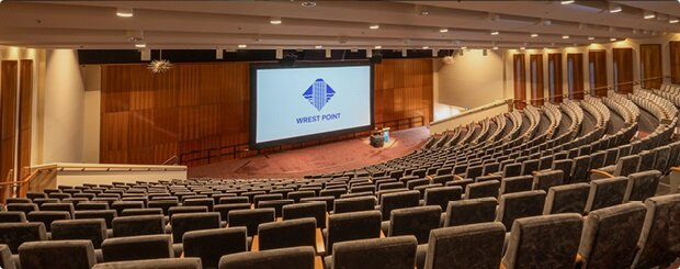 Large auditorium with rows of grey seats facing a stage with a big screen displaying the Wrest Point logo.